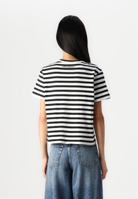 Camiseta corta de manga corta a rayas en blanco y negro con escote redondo. Presenta el logo "KARL LAGERFELD" en la parte posterior.