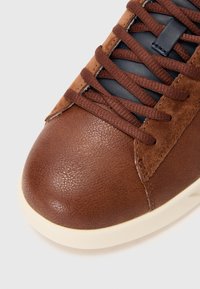 Baskets en cuir marron avec une finition texturée, des accents en suède, des lacets bleu marine et une semelle en caoutchouc de couleur crème.
