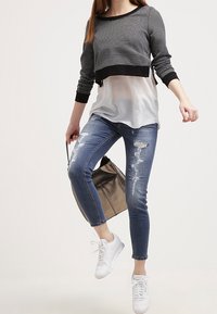 Pull court rayé noir et blanc porté par-dessus un top blanc superposé, associé à un jean skinny bleu déchiré et des baskets blanches. Sac cabas marron.