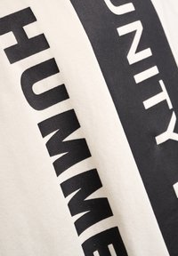 Hvid T-shirt med fed sort tekst i en vandret layout. Blød stoftekstur med en løs pasform. Minimalistisk design uden yderligere mønstre.