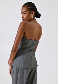 Top grigio senza spalline con un tessuto texturizzato, design aderente e cuciture verticali, abbinato a pantaloni larghi coordinati.