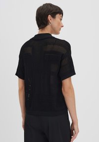 Schwarzes Poloshirt mit kurzen Ärmeln, das ein strukturiertes, offenes Strickdesign mit geometrischen Mustern, sowie einen gerippten Kragen und Bündchen aufweist.
