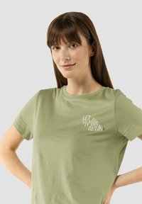 Olijfgroen katoenen t-shirt, korte mouwen, ronde hals, met op de voorkant een witte tekstafbeelding "LAAT DE ZON IN JE HART".