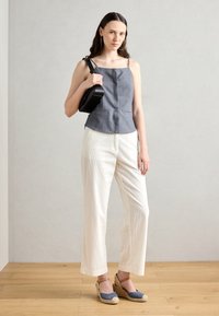Camiseta de lino azul con tirantes finos, pantalones de pierna ancha de punto blanco y cuñas de esparto azules. Modelo sosteniendo un bolso negro.