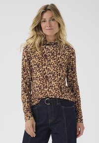 Halenka s leopardím vzorem a dlouhým rukávem s vyšším límcem, vyrobená z jemné látky v odstínech světlehnědé a burgundské, spárovaná s tmavými, vysokým pasem námořnickými džíny.