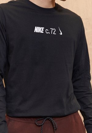 Schwarzes Langarm-T-Shirt aus Baumwolle, mit weißem Drucktext "NIKE c.72" und einem weißen Nike-Swoosh-Logo auf der Brust.
