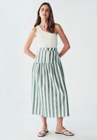 Biely rebrovaný tielko v kombinácii s maxi sukňou z ľanovej látky s vysokým pásom a pruhovaným dizajnom v zelenej a bielej farbe, doplnené bielymi sandálmi.