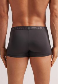 Grå boxershorts med en glat overflade og elastisk talje, der har et diskret logo. Designet er tæt og i midten af låret.