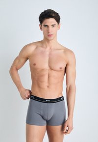 Boxers gris avec une ceinture élastique noire arborant le nom de la marque "BOSS." Texture lisse et design ajusté.