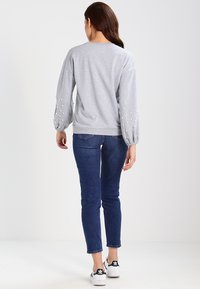 Šedá mikina s balónovými rukávy a perlovými ozdobami, kombinovaná s tmavě modrými skinny džíny a bílými teniskami. Jednoduchý, každodenní vzhled.