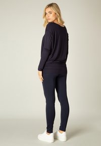 Marineblaues Langarmoberteil mit lockerer Passform, kombiniert mit marineblauen Leggings. Das Model trägt weiße Sneakers. Angenehmer Stoff, einfaches Design, keine sichtbaren Muster.