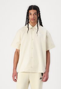 Κοντομάνικη, πουκαμίσα με κουμπιά σε παλ κίτρινο, κατασκευασμένη από ελαφρύ ύφασμα, με μικρό άσπρο λογότυπο στο στήθος και άνετη εφαρμογή.