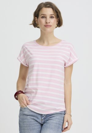 Rövid hajú nő, aki rózsaszín-fehér csíkos pólót, kék farmert, arany fülbevalókat, piros karkötőt és ezüst lánckarkötőt visel.