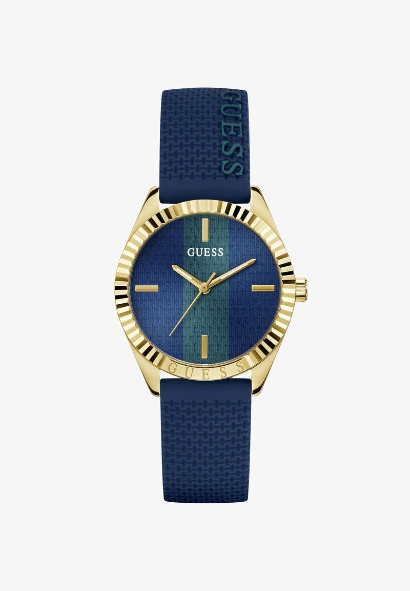 Montre couleur or avec cadran bleu texturé et bracelet en silicone bleu assorti, avec index dorés et marque "GUESS" sur le cadran et le bracelet.
