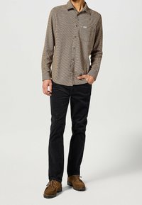 Brązowa koszula w kratę z długim rękawem, zapinana na guziki, z jedną kieszenią, w zestawieniu z czarnymi spodniami i brązowymi zamszowymi butami. Luźny krój.