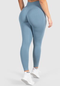 Leggings da yoga in morbido tessuto blu con vita alta, caratterizzati da un pannello testurizzato sulle cosce e abbinati a scarpe da ginnastica bianche.