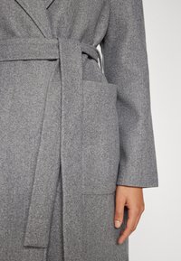 Γκρίζα παλτό από μίγμα μαλλιού με ζώνη, μακριά μανίκια και πατσί τσέπη στη αριστερή πλευρά. Μαλακή υφή και κομψός σχεδιασμός.