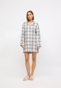 Grå och vit rutigt flanellklänningsskjorta med långa ärmar, knappar och krage, tillsammans med mjuka beige tofflor.