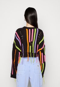 Pull en crochet noir avec des rayures verticales colorées en rose, vert, orange et violet, présentant des détails de franges et un design en maille ouverte.