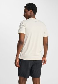 Lys beige t-shirt med kortærmer og rund hals. Har et lille blåt logo på ryggen, kombineret med sorte træningsshorts.