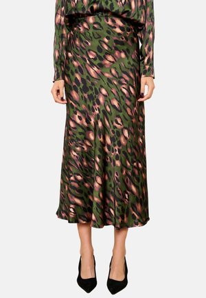 Woman wearing a green and pink abstract leopard-print midi skirt and matching long-sleeve top with black pointed-toe heels, standing on white background.