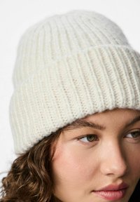 Berretto lavorato a maglia bianco con motivo a coste verticali e texture morbida, aderente alla testa, dotato di una corona semplice e arrotondata.