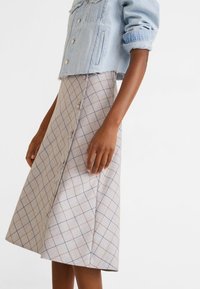 Veste en jean bleu clair raccourcie avec fermetures à boutons, associée à une jupe trapèze beige à carreaux avec des accents bleus et rouille et un détail de boutons à l'avant.