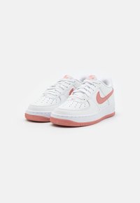 Bílé kožené sneakers Nike Air Force 1 s růžovými akcenty, které mají texturovanou gumovou podrážku, perforovaný špičky a ploché bílé tkaničky.