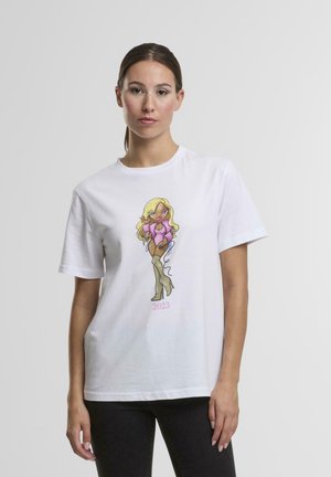 Femme avec les cheveux attachés portant un t-shirt blanc présentant une femme blonde de dessin animé en tenue rose et bottes hautes, avec le texte "2023" en dessous.