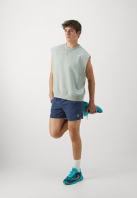Grå ermeløs hettegenser, marineblå shorts med Jordan-logo, og turkise treningssko. Glatt tekstur, uformelt design, egnet for sport.