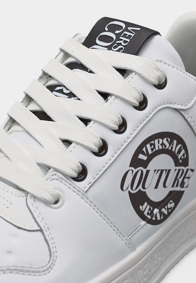 Бял маратонка White Versace Couture Jeans с бели връзки, черно лого отстрани и черна етикета с лого на езика.