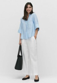 Ljust blå linneskjorta med avslappnad passform, vida ärmar och knappdetalj, tillsammans med vita linnestövlar med vida ben och svarta platta skor.