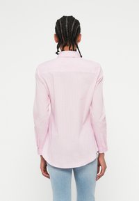 Camisa de manga longa com riscas em rosa claro e branco, em algodão. Corte ajustado com punhos abotoados e um bordo arredondado. Detalhes de costura visíveis.