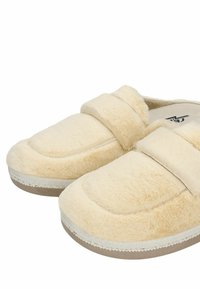 Crème-kleurige fuzzy slippers met een zachte textuur, voorzien van een platte zool, een ronde teen en een brede klittenbandsluiting over de bovenkant.