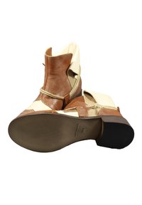 Stivaletti in pelle marrone con accenti crema, cuciture decorative e tacco spesso. Presentano una suola testurizzata e un dettaglio con cinturino regolabile.