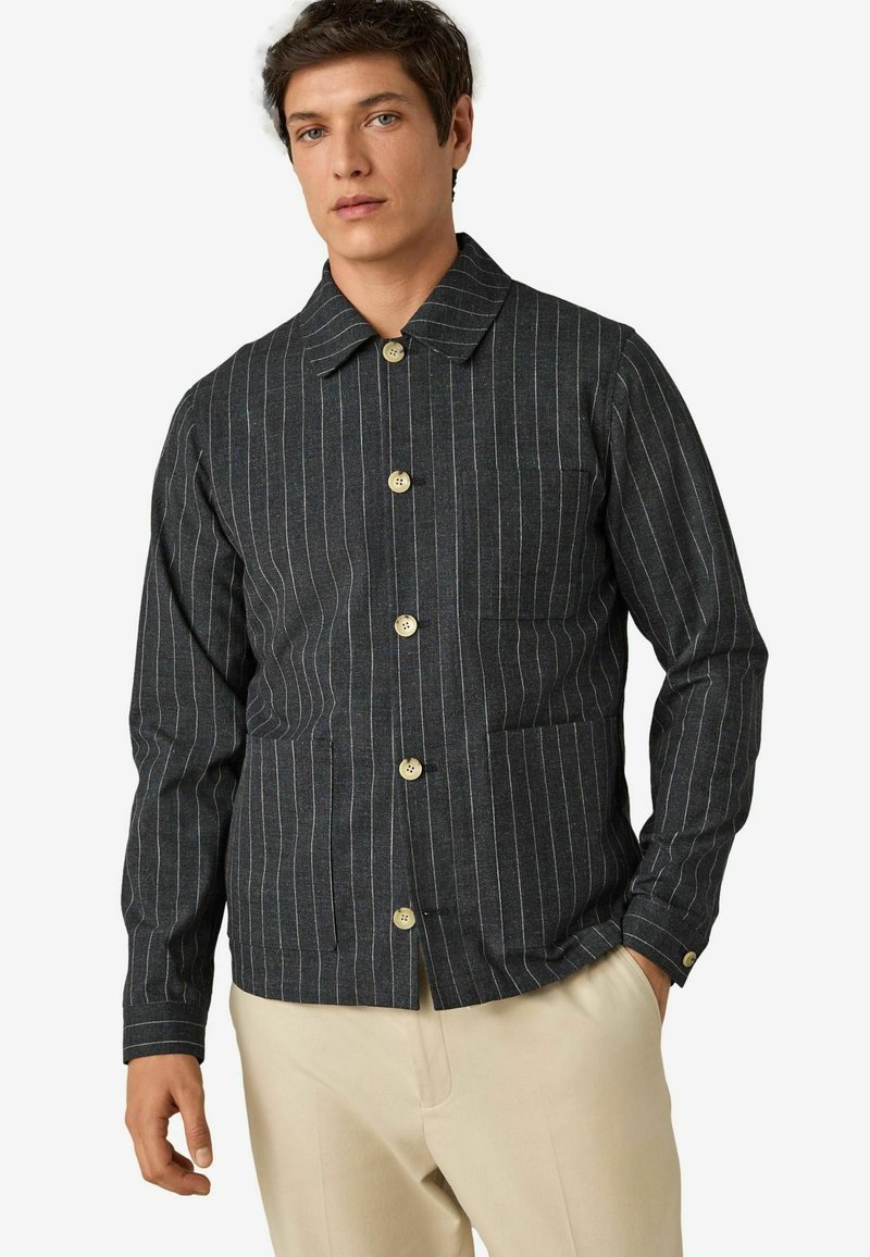 Tamno sivi prugasti sako s kragnom, pet dugmadi i prednjim džepom. Tkanina izgleda teksturirano; rukavi su dugi i uski.