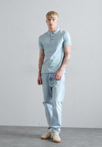 Svetlo modra polo majica z dvema gumboma, oblečena z svetlimu pranjem ravnimi džinsami in bež supergami. Preprost dizajn, minimalni vzorci, sproščen kroj.