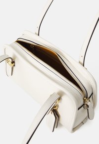 Sac bandoulière en cuir blanc avec double fermeture éclair, éléments dorés et deux étiquettes amovibles. Texture lisse et forme rectangulaire structurée.