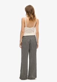 Top de punto de encaje en color crema con tirantes finos, combinado con pantalones de pierna ancha en blanco y negro con un diseño suelto y fluido.