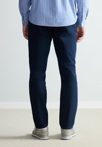Pantaloni ușori de culoare bleumarin, cu croială dreaptă. Materialul pare neted. Purtați cu adidași în nuanțe neutre. Mansetele cămășii și cusăturile sunt vizibile.