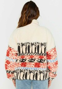 Pull-over en molleton crème avec un motif décoratif incluant des palmiers noirs, des accents rouges et bleus, et un col. Texture douce.