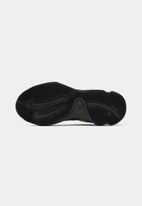 Sort tekstureret gummisål på en sportssko med mønstrede riller og et Nike-logo synligt på bunden.