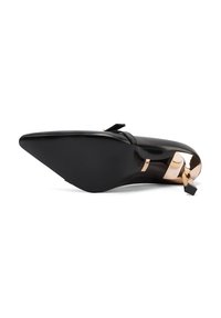 Scarpa nera in pelle con tacco alto e punta affilata, caratterizzata da un accento dorato sul tacco e un piccolo fiocco vicino alla cinghia.