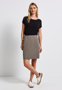 Haut noir à manches courtes, associé à une jupe grise avec deux poches avant et des accents de boutons. Porté avec des baskets blanches et beige.
