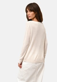 Jasno beżowy sweter z miękkiego materiału z długimi rękawami, z dekoltem w serek i luźnym krojem, zestawiony z białą spódnicą.