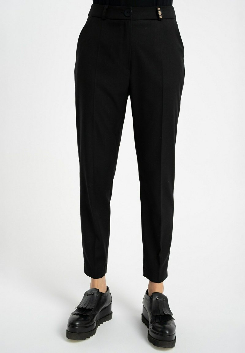 Czarne spódnie o dopasowanym kroju, z prostym przodem, bocznymi kieszeniami i lekko zwężającymi się nogawkami przy kostkach. Wykonane z gładkiego, lekkiego materiału.