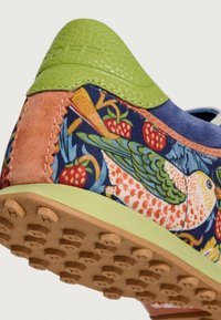 Scarpa multicolore con motivo floreale e uccelli su tessuto, dettagli in pelle verde e suola in gomma testurizzata con chiodini antiscivolo.