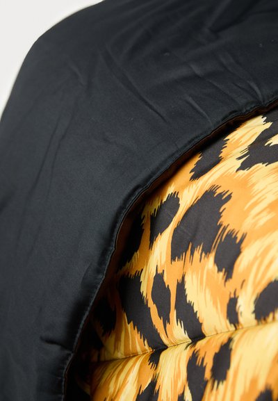Black fabric covers a padded cushion with an orange and black leopard print pattern, featuring soft textures and rounded edges.
