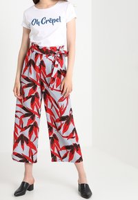 Vit t-shirt med texten "Oh Crêpe!" i blått, ihop med vida grå byxor som har ett röd- och svart mönster av blommor. Svarta klackskor.
