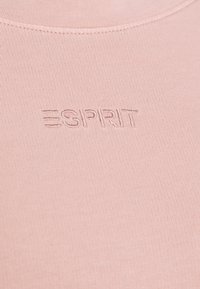 Close-up van een roze stof met het gestikte "ESPRIT" logo in dezelfde kleur draad onder een ronde halslijn.